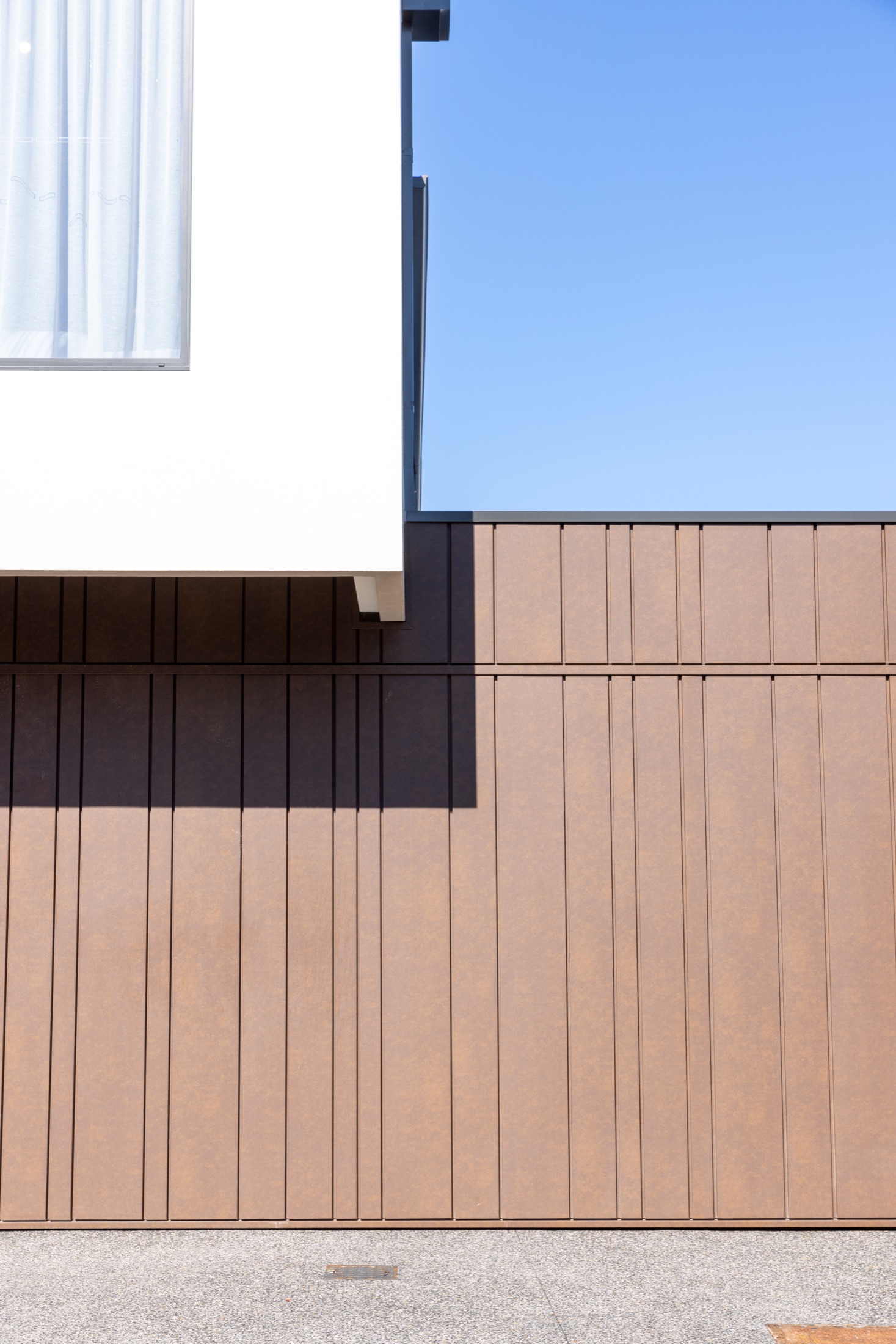 Close view of the bronze vertical cladding and rendered upper storey