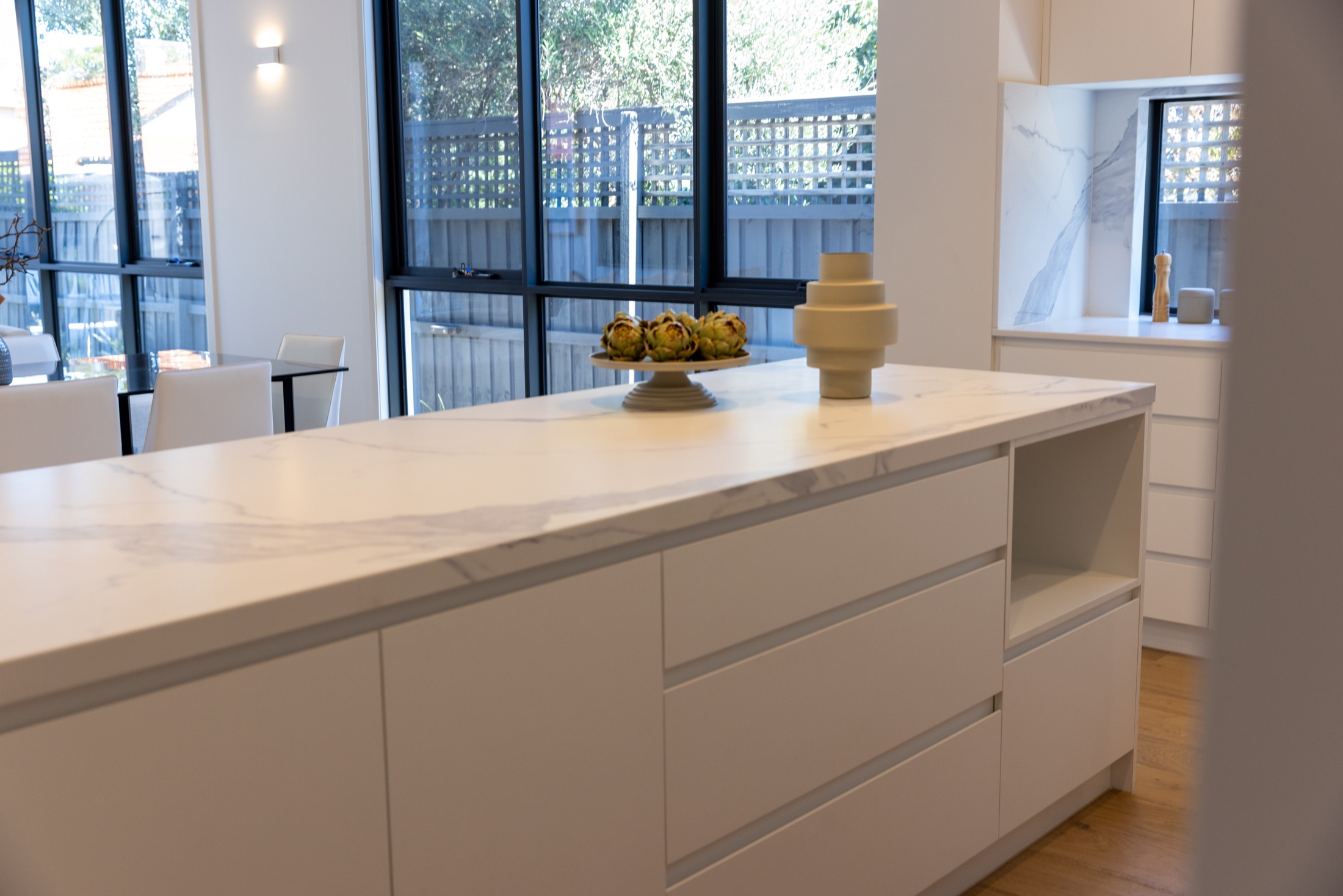 Kitchen island with stone benchtop beside full-height black framed windows